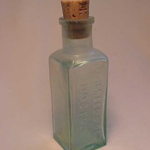 May include: A small, clear glass bottle with a cork stopper. The bottle is embossed with the text "THREE STAR" and "ROSTOCK".