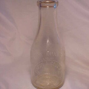 May include: A clear glass milk bottle with a one quart capacity. The bottle has a label that reads "Spring Valley Dairy Co.  One Quart  Glass".