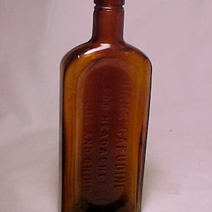 May include: A brown glass bottle with a glass stopper. The bottle is labeled "HUCK'S CAPUDINE FOR HEADACHES & GRIPPE".