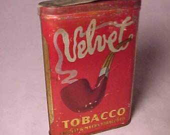 Può includere: Una scatola vintage di tabacco Velvet con sfondo rosso e lettere dorate. La scatola presenta un'immagine stilizzata di una pipa con fumo che si arriccia verso l'alto. Il testo "Velvet Tobacco" è stampato sulla parte anteriore della scatola.