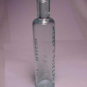 May include: A clear glass bottle with a green tint. The bottle is labeled "W. H. KLA 1880 INDIAN OIL" and "W. H. SICE LEN'S"