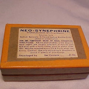 May include: An antique rectangular box with an orange frame and a tan label. The label reads "NEO-SYNEPHRINE HYDROCHLORIDE" and provides instructions for use. The box is likely for nasal congestion relief.