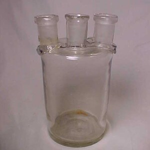 May include: A clear glass laboratory bottle with three openings on the top. The bottle is cylindrical and has a round bottom.