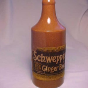 May include: A brown glass bottle with a label that reads "Schweppes Ginger Beer".