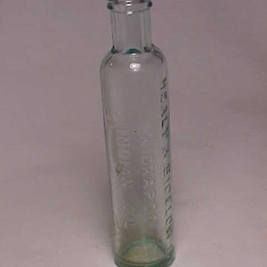 May include: A clear glass bottle with a green tint. The bottle has a narrow neck and a rounded bottom. The text "HEALY & EICHELBERGER'S" is etched into the side of the bottle.