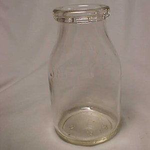 May include: A clear glass bottle with a rounded bottom and a slightly flared top. The bottle has a textured rim and a smooth, clear body.