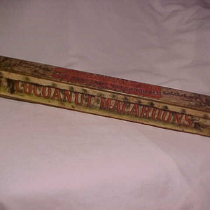 May include: A vintage tin box with a faded, yellowed label that reads "COCANUT MACAROONS". The box is rectangular and has a slightly worn, aged appearance.