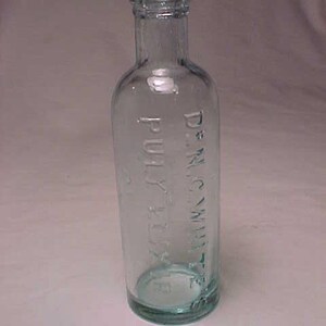 May include: A clear glass bottle with a textured surface. The bottle has the text "Dr. M.C. White's Pulvex Flea" printed on it.