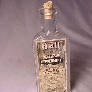 May include: A clear glass bottle with a cork stopper. The label reads "Hall Brand EXTRACT PEPPERMINT" with additional text about the product's strength and ingredients. The bottle is rectangular with rounded edges.