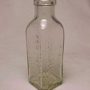 May include: A clear glass bottle with a square shape and a textured surface. The bottle has the text "DR. BULL'S" and "1/2 OZ" embossed on the sides.