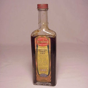 May include: A glass bottle with a red cap and a yellow label that reads "Health-O Quality Products" and "Imitation Lemon Syrup".