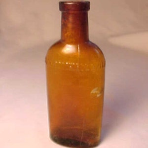 May include: A small, amber-colored glass bottle with a rounded bottom and a narrow neck. The bottle is empty and has a slightly textured surface.