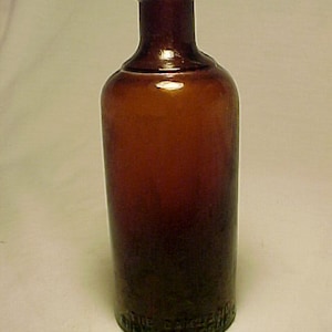 May include: A dark brown glass bottle with a rounded bottom and a narrow neck. The bottle has a label that reads "The Original Dickens Liver Medicine".