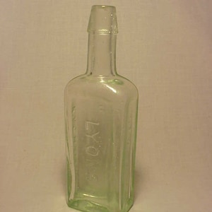 May include: A clear glass bottle with a rounded top and a square body. The bottle is embossed with the word "ROYAL" on the front.