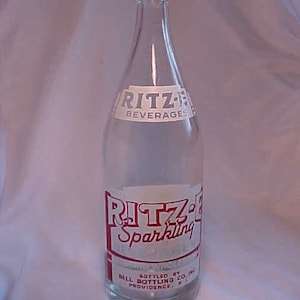 May include: A clear glass bottle with a red and white label that reads "Ritz's Sparkling Beverages Bottled By Bell Bottling Co., Inc. Providence, R.I."