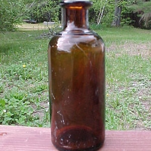 May include: A dark brown glass bottle with a wide mouth and a rounded bottom. The bottle is sitting on a wooden surface.