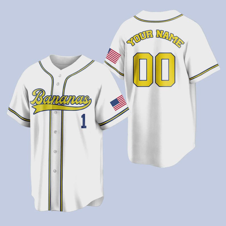 Op de afbeelding: Wit honkbalshirt met "Bananas" in gele letters over de borst en het nummer 1 in blauw. De achterkant heeft "YOUR NAME" en het nummer 00 in geel. Amerikaanse vlagpatches staan op de mouwen.