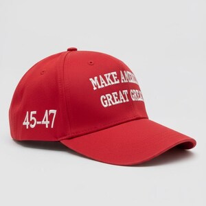 May include: A red baseball cap with the text "MAKE AMERICA GREAT AGAIN" in white block letters. The number "45-47" is printed on the side of the cap in white. The cap has a curved brim and a button on top.