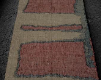 May include: A rectangular rug with a beige background and three red rectangular shapes. The red shapes are outlined with a dark blue-green color. The rug has a fringe on the short end.