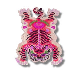 May include: A colorful, decorative tiger rug with a unique design. The rug features a vibrant color palette of pink, purple, and black, with floral and patterned details. The tiger's face has a skull-like appearance, adding a distinctive touch.