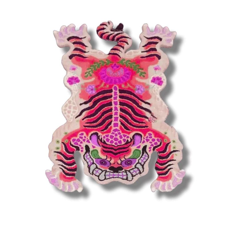 May include: A colorful, decorative tiger rug with a unique design. The rug features a vibrant color palette of pink, purple, and black, with floral and patterned details. The tiger's face has a skull-like appearance, adding a distinctive touch.
