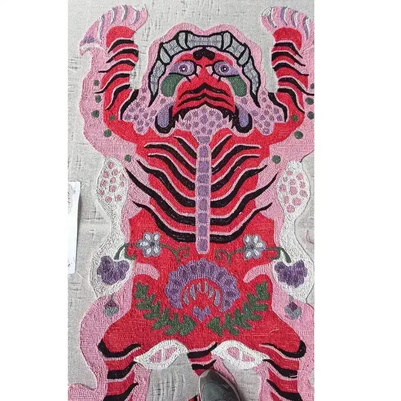 May include: A vibrant, hand-stitched rug featuring a stylized tiger design. The rug showcases a red tiger with black stripes, purple accents, and a pink border. Floral details and intricate patterns add to the rug's decorative appeal.