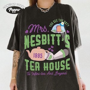 May include: Dark gray Comfort Colors t-shirt with a graphic design. The design features the text "Mrs. Nesbitt's Tea House" in green and purple, along with a teapot, the year 1995, and the phrase "To Infini-tea And Beyond."