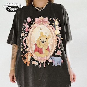 May include: Dark grey Comfort Color t-shirt with a framed illustration of Winnie the Pooh and friends. The design includes pink bows, flowers, and a bee. The shirt has the text "Comfort Color Pepper" at the top left.