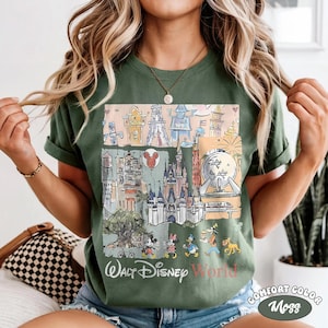 Peut inclure: T-shirt vert avec une illustration color&eacute;e des monuments et personnages de Walt Disney World. Le motif comprend des images du ch&acirc;teau de Cendrillon, de Spaceship Earth et de Mickey Mouse. Les mots "Walt Disney World" sont imprim&eacute;s en bas.