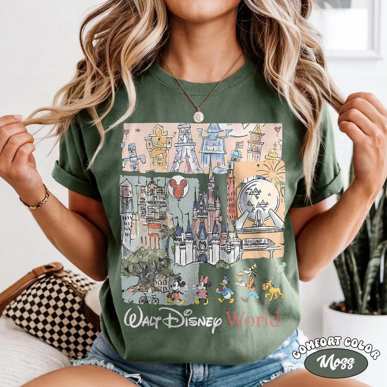 Peut inclure: T-shirt vert avec une illustration color&eacute;e des monuments et personnages de Walt Disney World. Le motif comprend des images du ch&acirc;teau de Cendrillon, de Spaceship Earth et de Mickey Mouse. Les mots "Walt Disney World" sont imprim&eacute;s en bas.