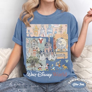 Peut inclure: T-shirt bleu Comfort Color avec un graphisme color&eacute; des monuments et personnages de Walt Disney World. Le motif comprend le texte "Walt Disney World" dans une police stylis&eacute;e, avec Mickey et Minnie Mouse, Donald Duck, Dingo et Pluto.