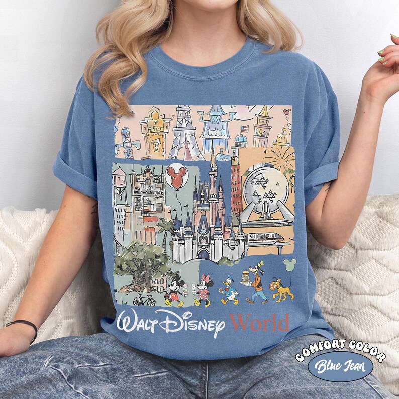 Peut inclure: T-shirt bleu Comfort Color avec un graphisme color&eacute; des monuments et personnages de Walt Disney World. Le motif comprend le texte "Walt Disney World" dans une police stylis&eacute;e, avec Mickey et Minnie Mouse, Donald Duck, Dingo et Pluto.