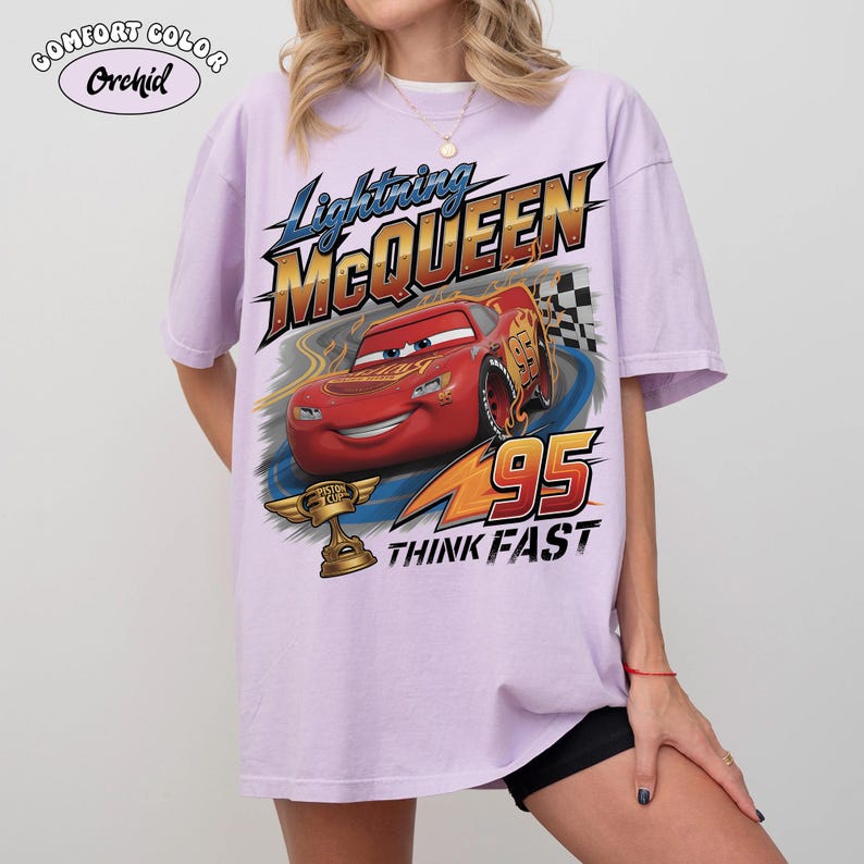 Op de afbeelding: Lichtpaars T-shirt met een afbeelding van Lightning McQueen uit de film Cars. De afbeelding bevat de tekst "Lightning McQueen", "95" en "Think Fast", samen met een afbeelding van de rode raceauto en een trofee.