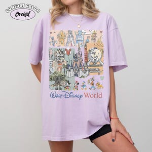 Peut inclure: Un t-shirt lilas avec un motif color&eacute; des monuments et personnages de Walt Disney World. Le t-shirt porte l'inscription "Walt Disney World" dans une police stylis&eacute;e. Le coin sup&eacute;rieur gauche du t-shirt porte l'inscription "Comfort Color Orchid".
