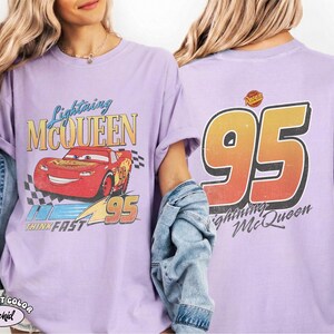 Puede incluir: Camiseta de color lila con un dise&ntilde;o de Rayo McQueen de la pel&iacute;cula Cars. El frente muestra a McQueen, el texto "Lightning McQueen" y "95". La parte trasera presenta un gran "95" y el texto "Lightning McQueen".