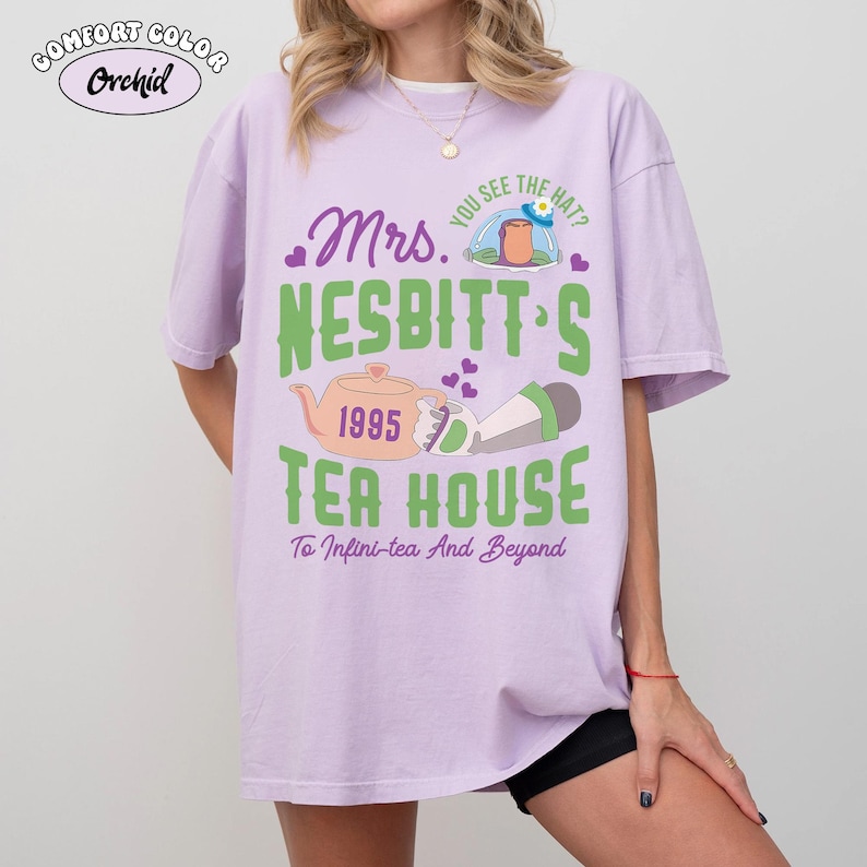 May include: A light purple Comfort Colors t-shirt with the text "Mrs. Nesbitt's Tea House 1995" in green and orange. The shirt features a teapot graphic and the phrase "To Infini-tea And Beyond". The shirt also has the text "You see the hat?" above the tea house graphic.