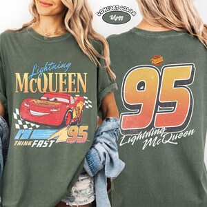Puede incluir: Camiseta verde con Lightning McQueen de la pel&iacute;cula Cars. El frente muestra el personaje y los textos "Lightning McQueen", "Think Fast" y "95". La parte trasera presenta un gran "95" y el texto "Lightning McQueen".