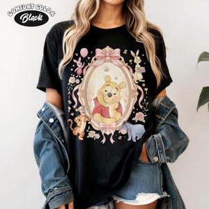 May include: Black t-shirt with a framed illustration of Winnie the Pooh, pink bows, and other characters. The shirt has the text "Comfort Color Black" in a circular design at the top left.