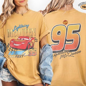 Puede incluir: Camiseta de color mostaza con Lightning McQueen de la pel&iacute;cula Cars. El gr&aacute;fico frontal muestra el coche de carreras rojo con el texto "Lightning McQueen" y "95". La parte trasera de la camiseta muestra un gran "95" y el texto "Lightning McQueen".