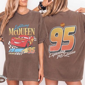 Puede incluir: Camiseta marr&oacute;n con Lightning McQueen de la pel&iacute;cula Cars. La parte delantera muestra un dise&ntilde;o de coche de carreras rojo con el texto "Lightning McQueen" y "95". La parte trasera muestra un gran "95" con "Lightning McQueen" debajo.