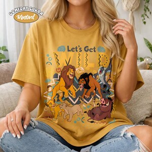 May include: Mustard-colored t-shirt with the text "Let's Get WILD" and a graphic featuring cartoon lions, a warthog, and a monkey. The shirt is a Comfort Color brand.