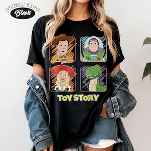 May include: Black Comfort Colors t-shirt featuring four cartoon character portraits from Toy Story: Woody, Buzz Lightyear, Jessie, and Rex. The words "TOY STORY" are printed in yellow below the portraits. The shirt has a crew neck.
