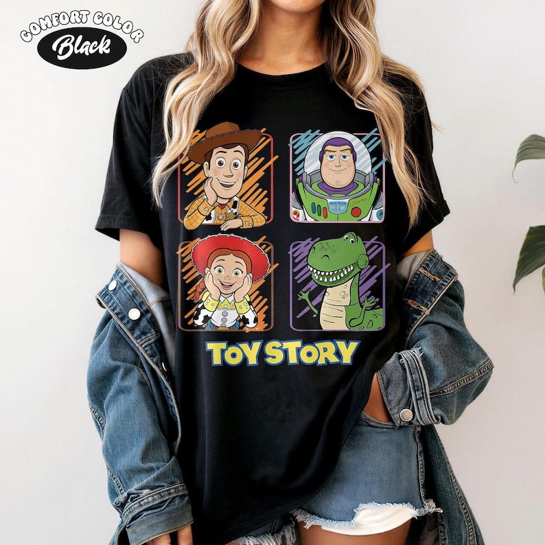 May include: Black Comfort Colors t-shirt featuring four cartoon character portraits from Toy Story: Woody, Buzz Lightyear, Jessie, and Rex. The words "TOY STORY" are printed in yellow below the portraits. The shirt has a crew neck.