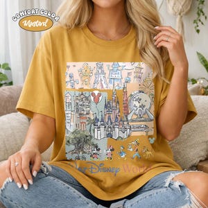 Peut inclure: T-shirt Comfort Color moutarde avec un graphisme color&eacute; des monuments et personnages de Disney World. Le motif comprend des ch&acirc;teaux, un ballon Mickey Mouse et les mots "Disney World".