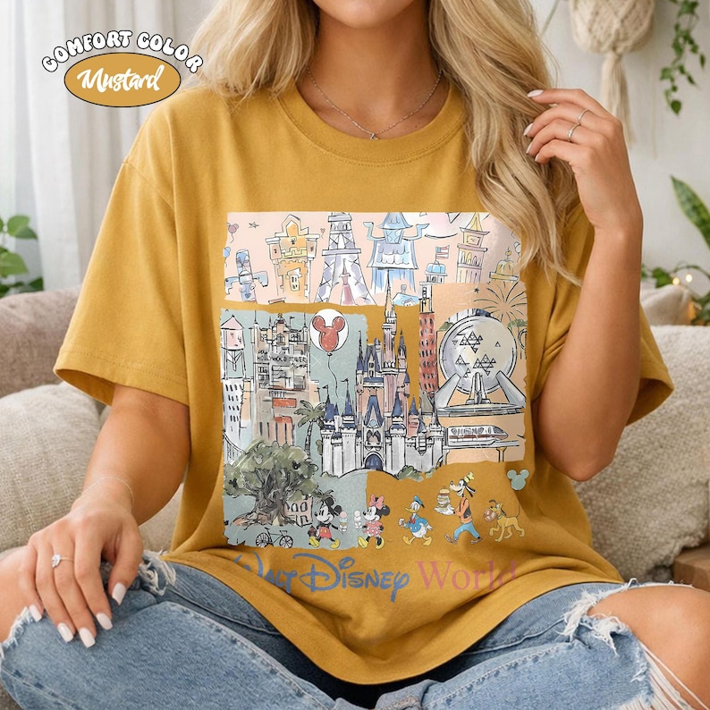 Peut inclure: T-shirt Comfort Color moutarde avec un graphisme color&eacute; des monuments et personnages de Disney World. Le motif comprend des ch&acirc;teaux, un ballon Mickey Mouse et les mots "Disney World".