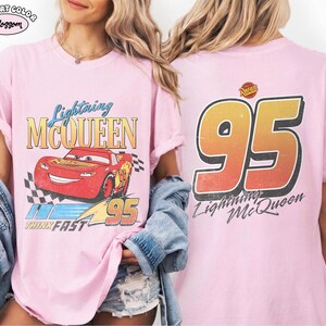 Puede incluir: Camiseta rosa claro con Lightning McQueen de la pel&iacute;cula Cars. El frente muestra el personaje, texto y una bandera a cuadros. La parte posterior muestra un gran "95" y las palabras "Lightning McQueen".