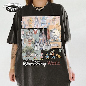 Peut inclure: T-shirt gris fonc&eacute; Comfort Colors avec un graphisme color&eacute; des monuments et personnages de Walt Disney World. Le motif comprend Mickey Mouse, Minnie Mouse, Donald Duck, Dingo et Pluto. Les mots "Walt Disney World" sont imprim&eacute;s en dessous.