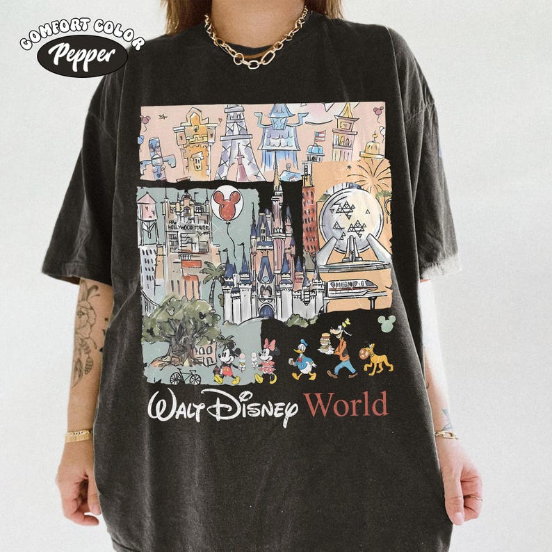 Peut inclure: T-shirt gris fonc&eacute; Comfort Colors avec un graphisme color&eacute; des monuments et personnages de Walt Disney World. Le motif comprend Mickey Mouse, Minnie Mouse, Donald Duck, Dingo et Pluto. Les mots "Walt Disney World" sont imprim&eacute;s en dessous.