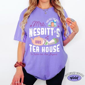 May include: A violet Comfort Colors t-shirt with a graphic design. The design includes the text "Mrs. Nesbitt's Tea House" with a teapot illustration and the phrase "To Infini-tea And Beyond."