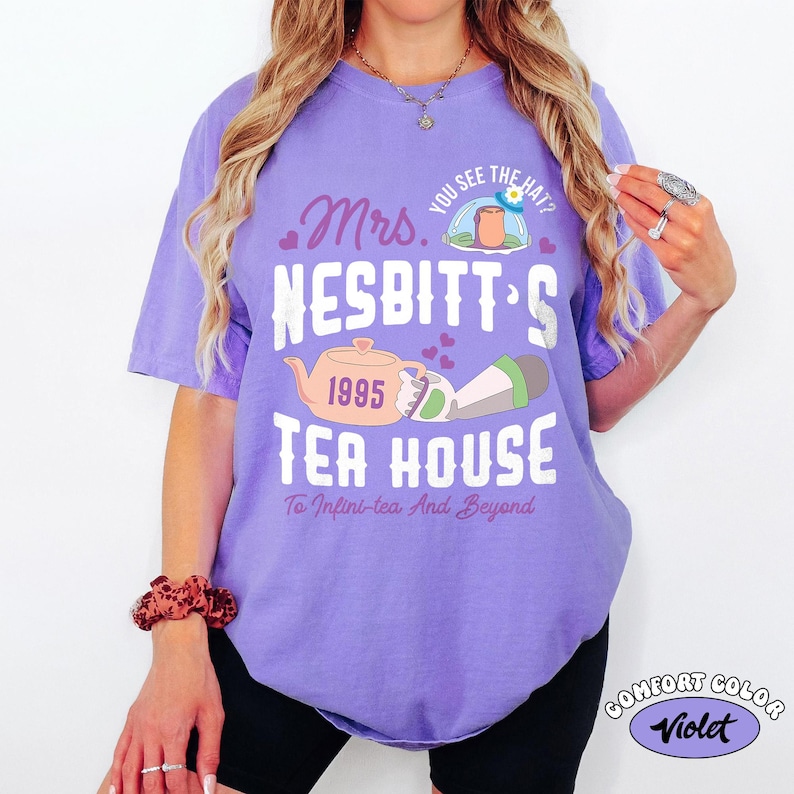 May include: A violet Comfort Colors t-shirt with a graphic design. The design includes the text "Mrs. Nesbitt's Tea House" with a teapot illustration and the phrase "To Infini-tea And Beyond."